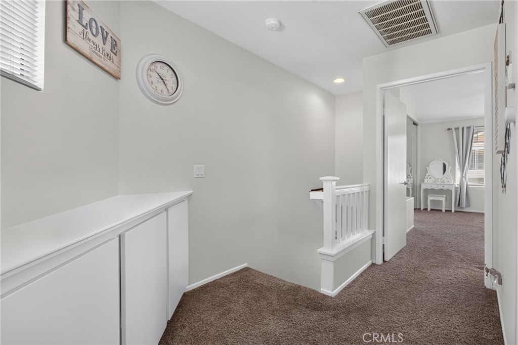 Carpeted upstairs landing with white built-in cabinets, a stair railing, and an open doorway to a bedroom.