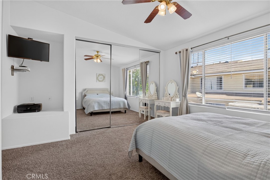 Bedroom with mirrored closet doors, a ceiling fan, and large windows overlooking a neighboring home.