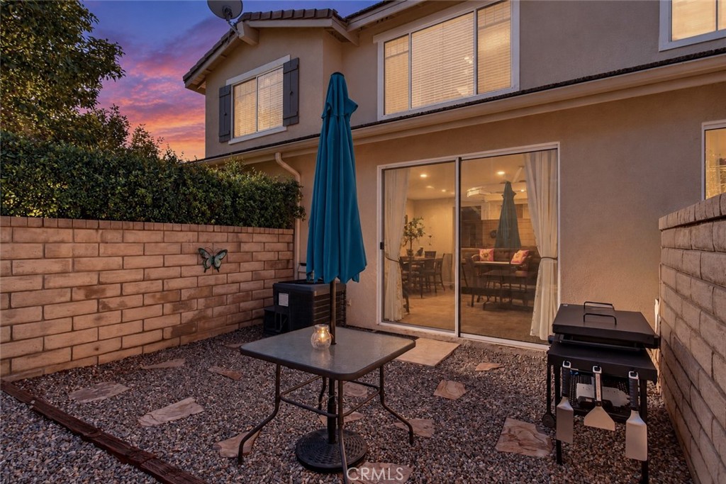 Two-story home's gravel backyard patio with a table, closed umbrella, and grill at dusk.