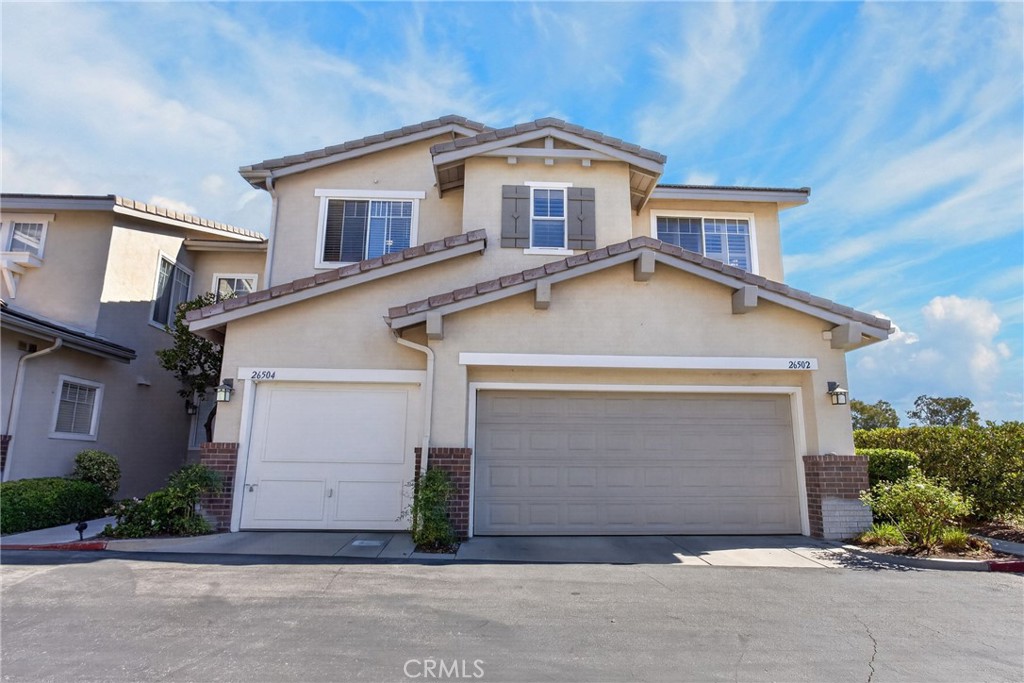 Two-story stucco residence with tiled gables, two garage doors, and a blue sky.