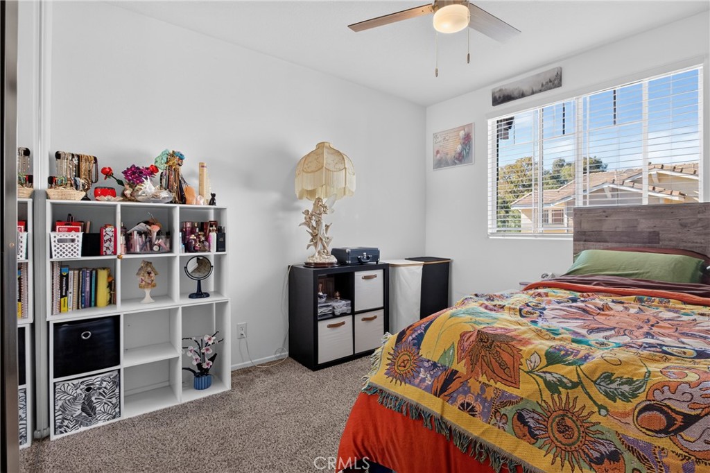 Bedroom with a colorful patterned bedspread, white shelving, and a large window with blinds.