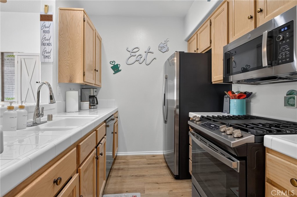 Kitchen with light wood cabinets, white counters, stainless steel appliances, and a gas range.