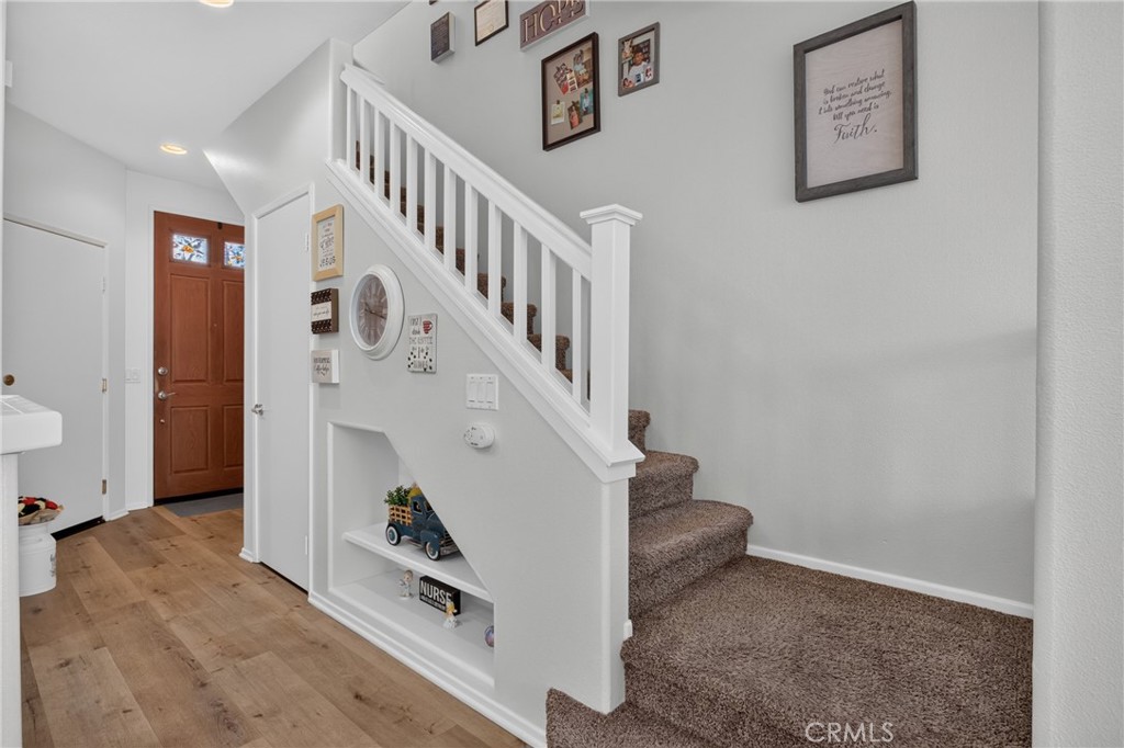 Entryway with a carpeted staircase, white railing, wood flooring, and built-in display shelves.