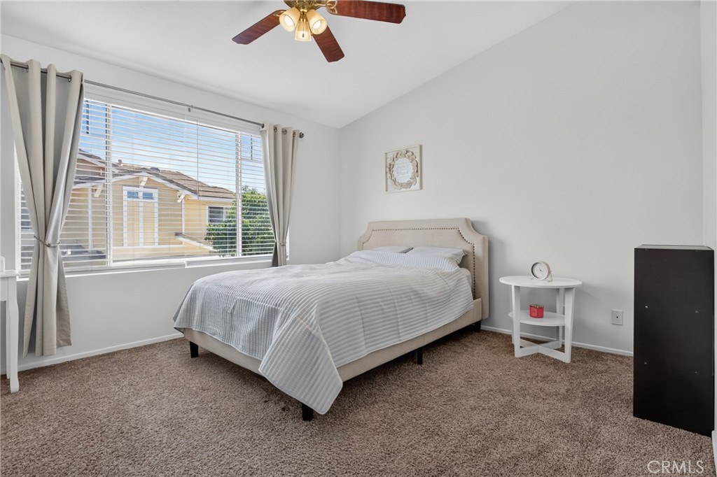 Bright staged bedroom with a striped bedspread, large curtained window, and ceiling fan.