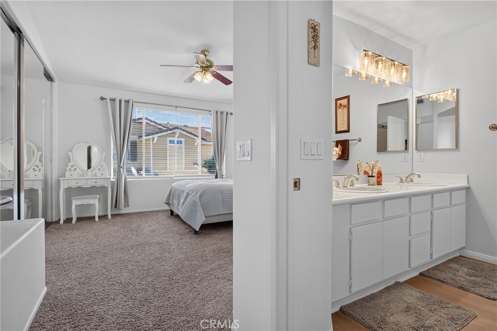 Bedroom with a window-side bed and vanity, adjoining a bathroom with a double-sink cabinet.