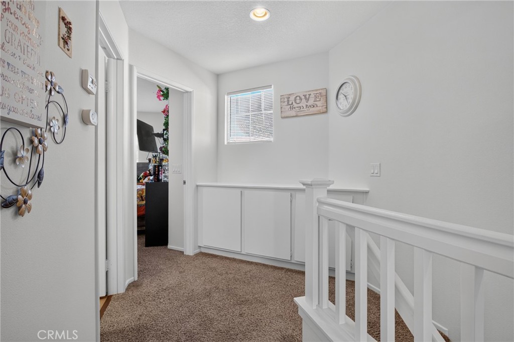 Upstairs hallway with carpeted floors, white stair railing, built-in cabinets, and a small window.