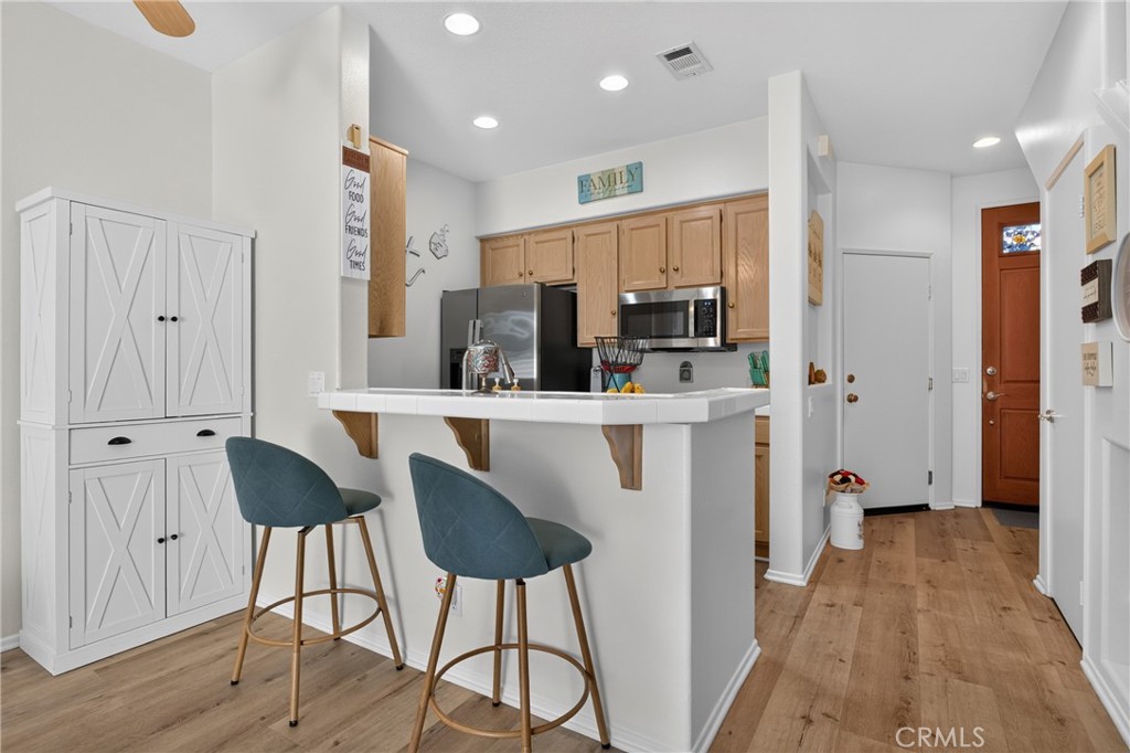 Kitchen with a white breakfast bar, blue stools, and light wood cabinets.