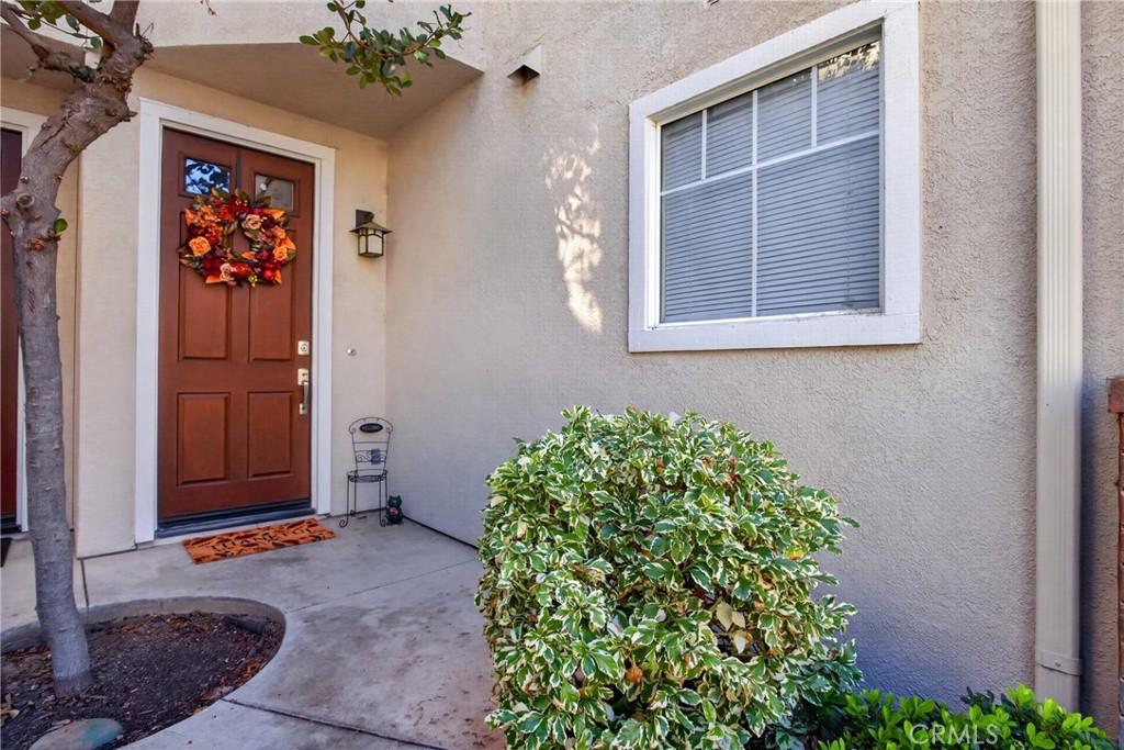 Home entrance with a wreath-covered wooden door, window, and front shrubs.