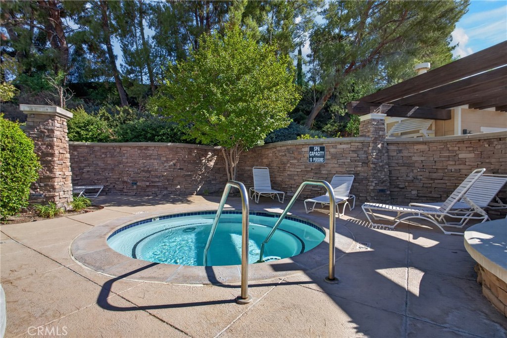 Circular spa with metal handrails, lounge chairs, and a stone privacy wall.