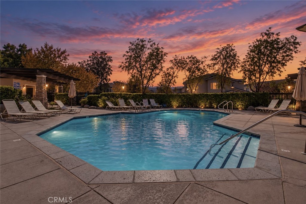 Community swimming pool with lounge chairs beneath a colorful sunset sky.