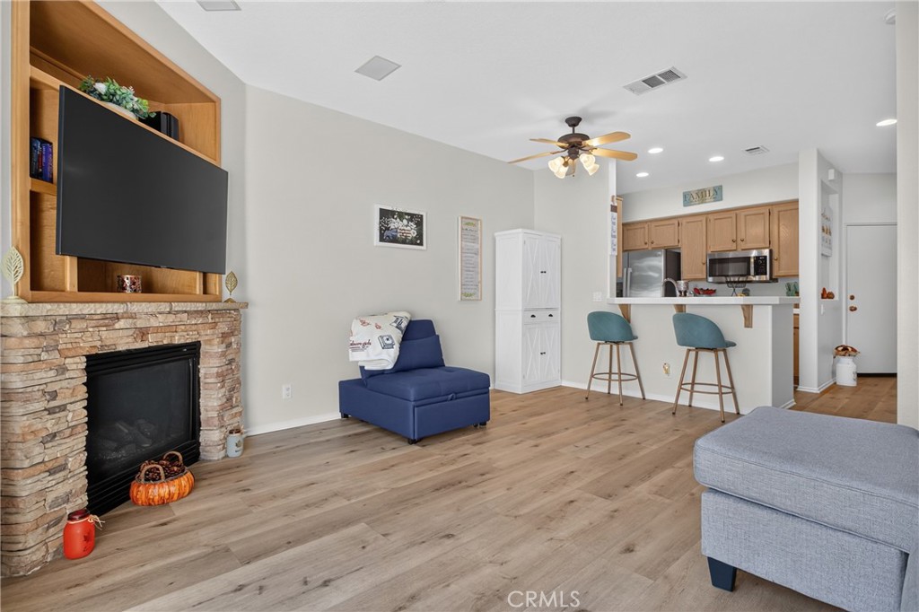 Living room with stone fireplace, built-in TV, blue chair, and an open kitchen with a breakfast bar.