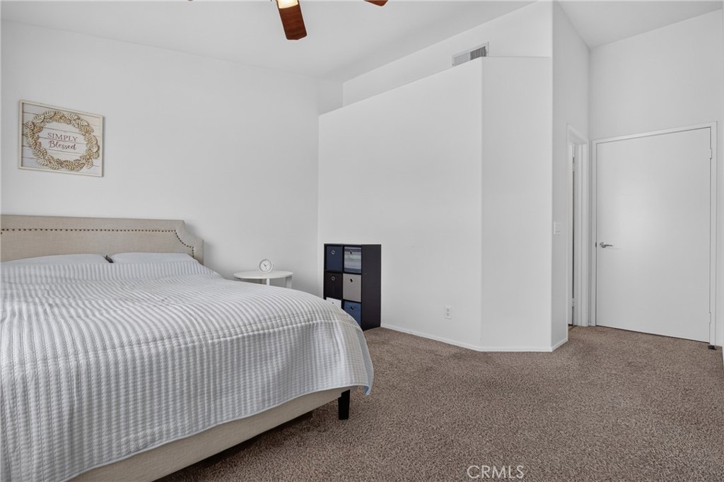 Bedroom with a large bed, beige carpet, and a small bedside table.