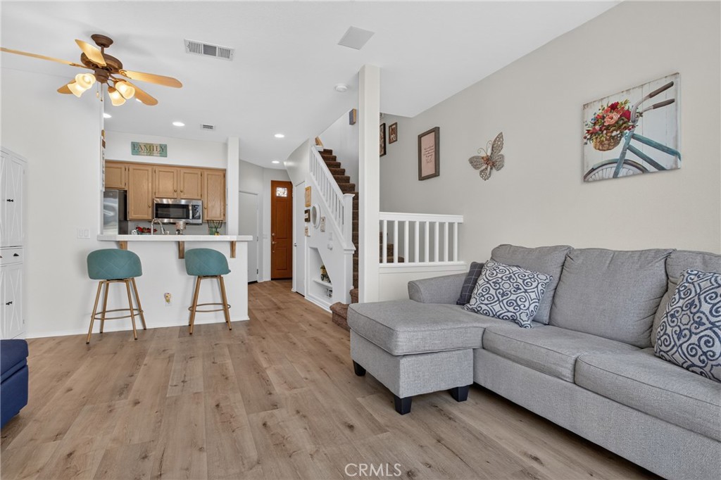 Living room with gray sectional, wood floors, and open kitchen with breakfast bar.