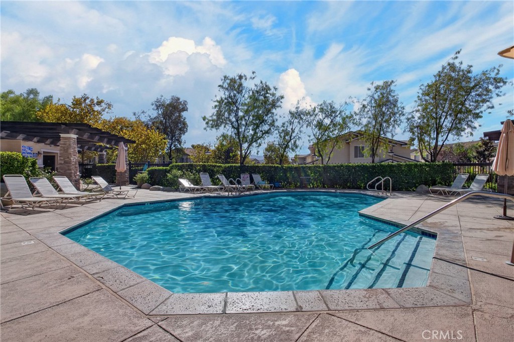 Community swimming pool with stone patio, lounge chairs, and a shaded pergola.