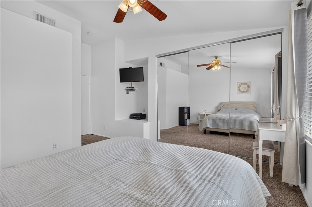 Bedroom with mirrored closet doors, a ceiling fan, and a bed beside a window.