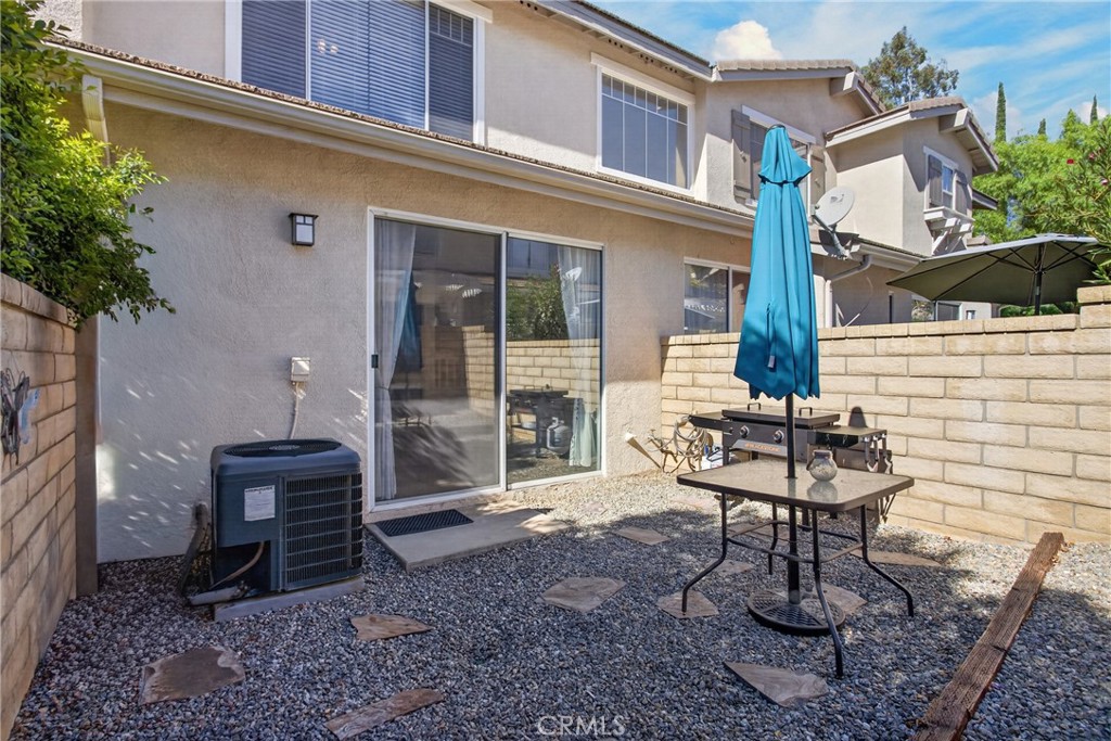 Rear patio with gravel ground, sliding glass doors, outdoor table, grill, and blue umbrella.