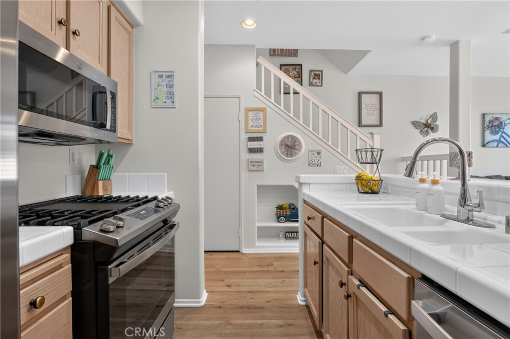 Kitchen with gas range, stainless microwave, white counters, and wood cabinetry overlooking a staircase.