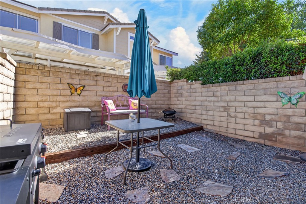 Enclosed gravel patio with a table, teal umbrella, pink bench, and barbecue grill.