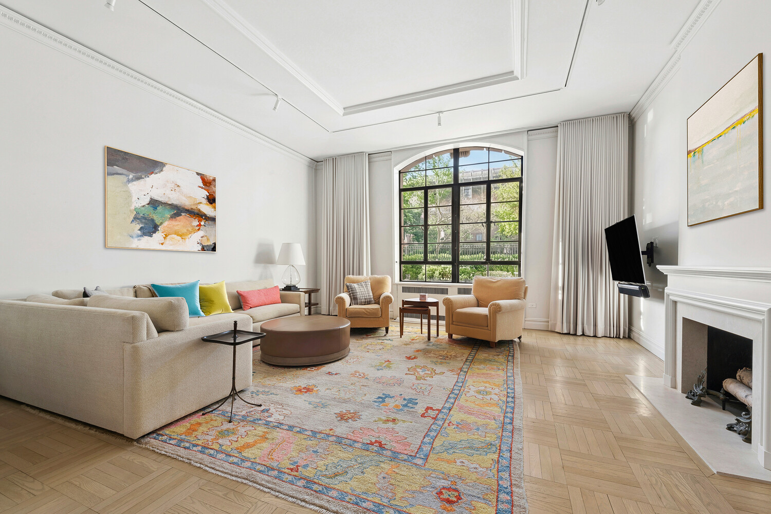 Living room with an arched window, cream seating, colorful rug, and fireplace.