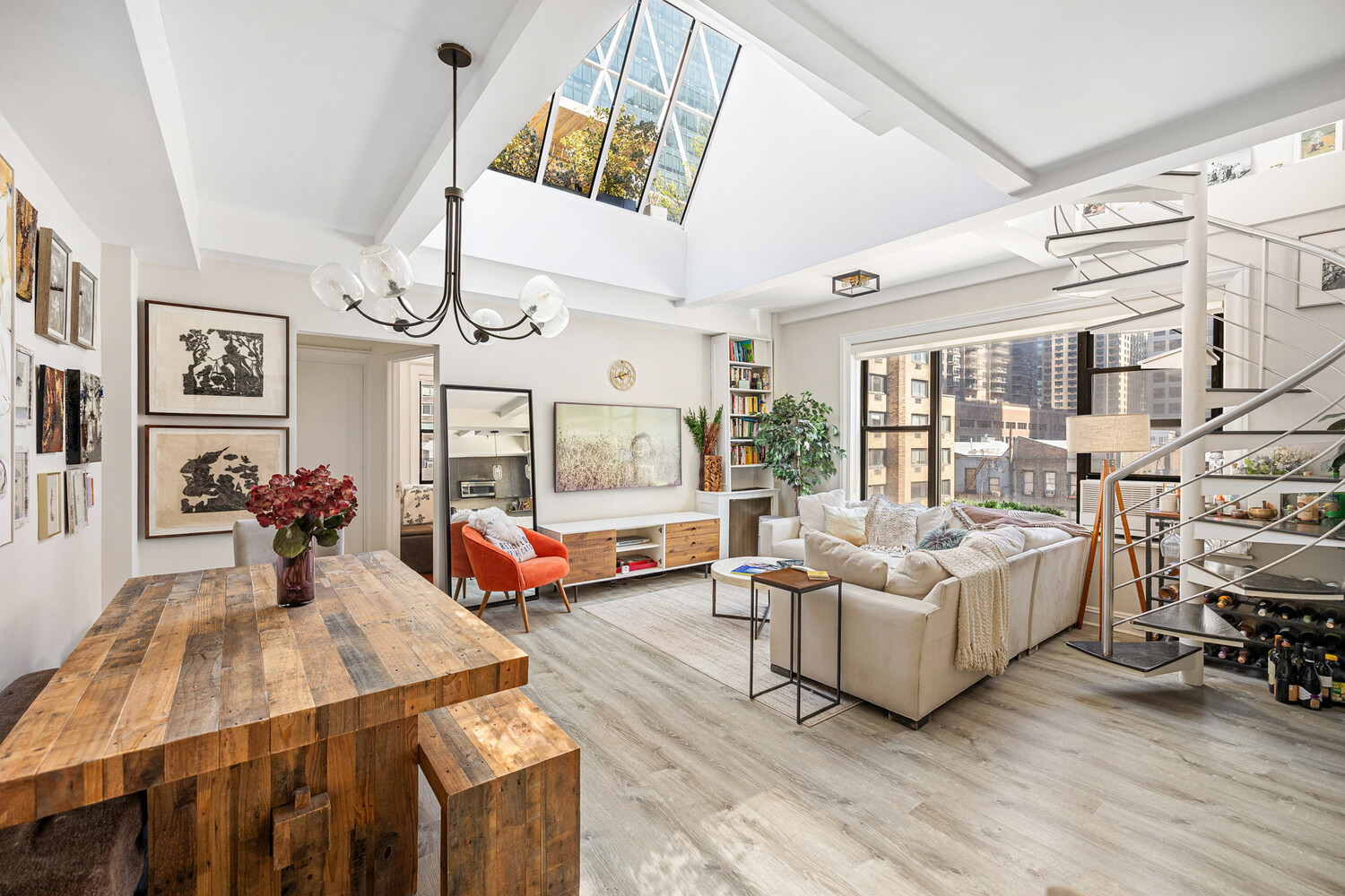 Open living and dining area with a vaulted skylight, city views, white sectional, and spiral staircase.