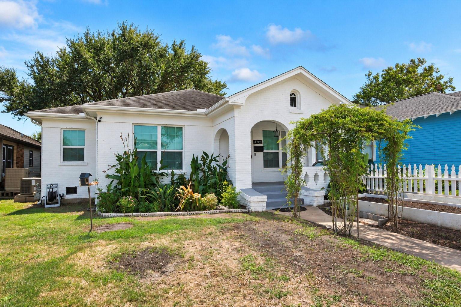 White brick house with an arched entry, front garden, and white picket fence.