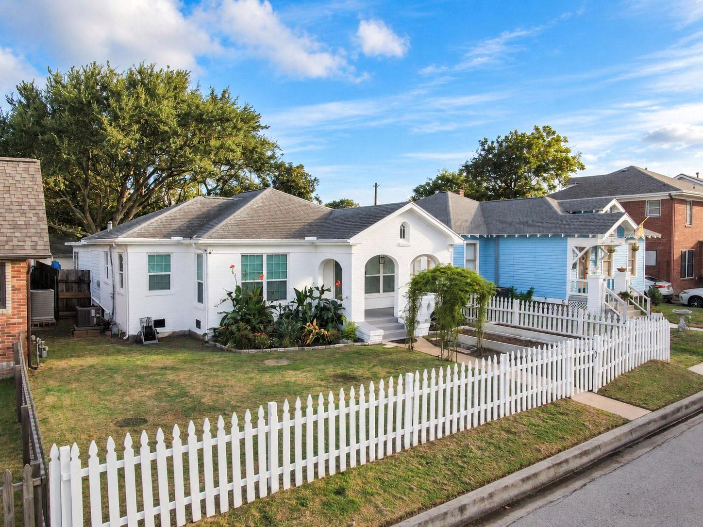 White brick house with arched entryways, front garden, and a white picket fence.