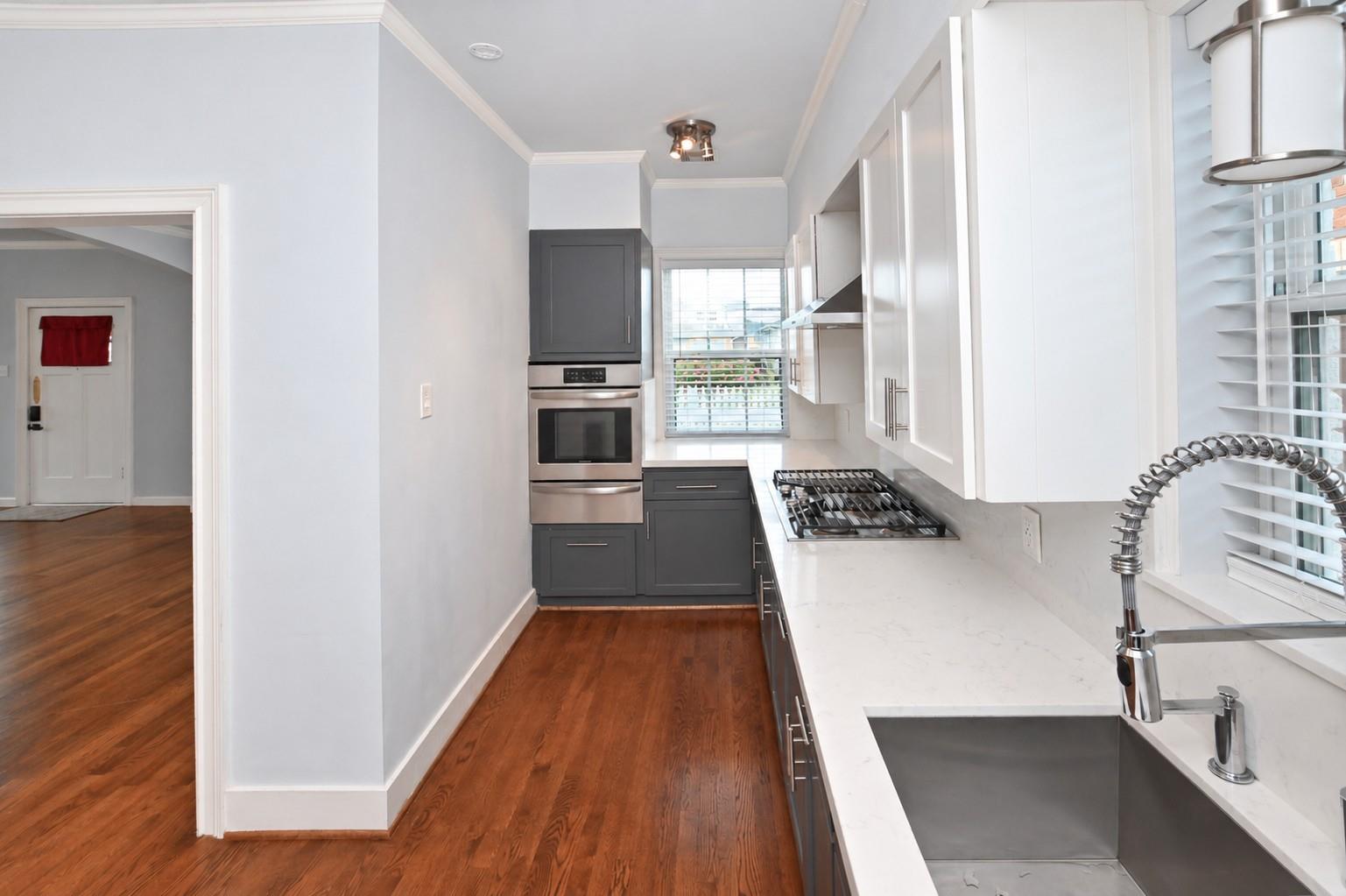 Galley kitchen with white counters, gray cabinets, stainless appliances, and hardwood floors.