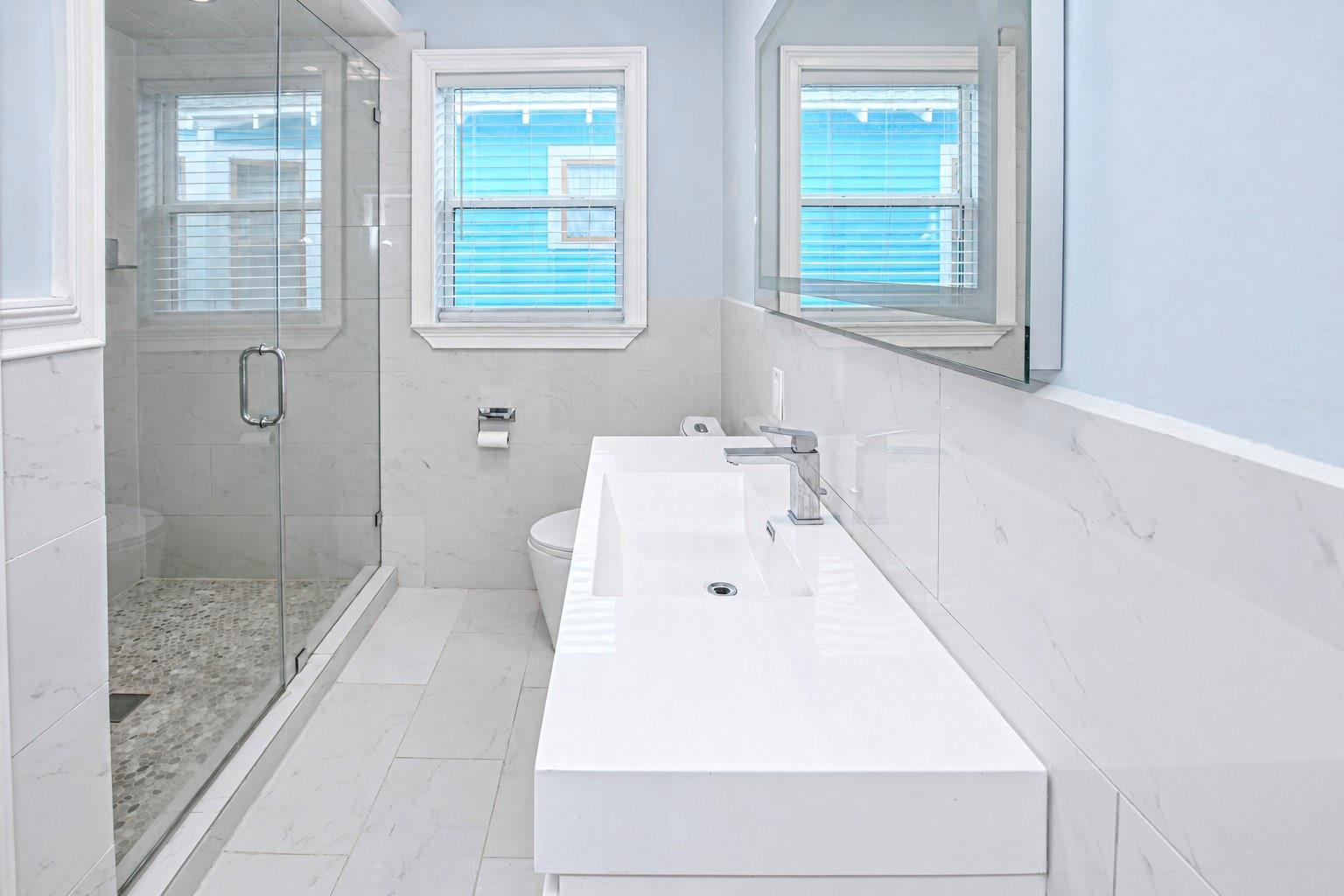 Modern bathroom with a glass shower, pebble floor, marble-look tile, and long white vanity.