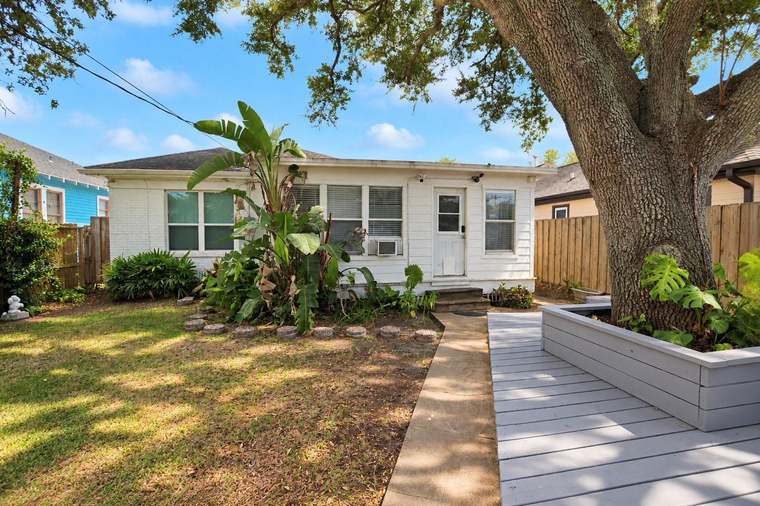 Rear of a white single-story house with a gray deck beneath a large mature tree.