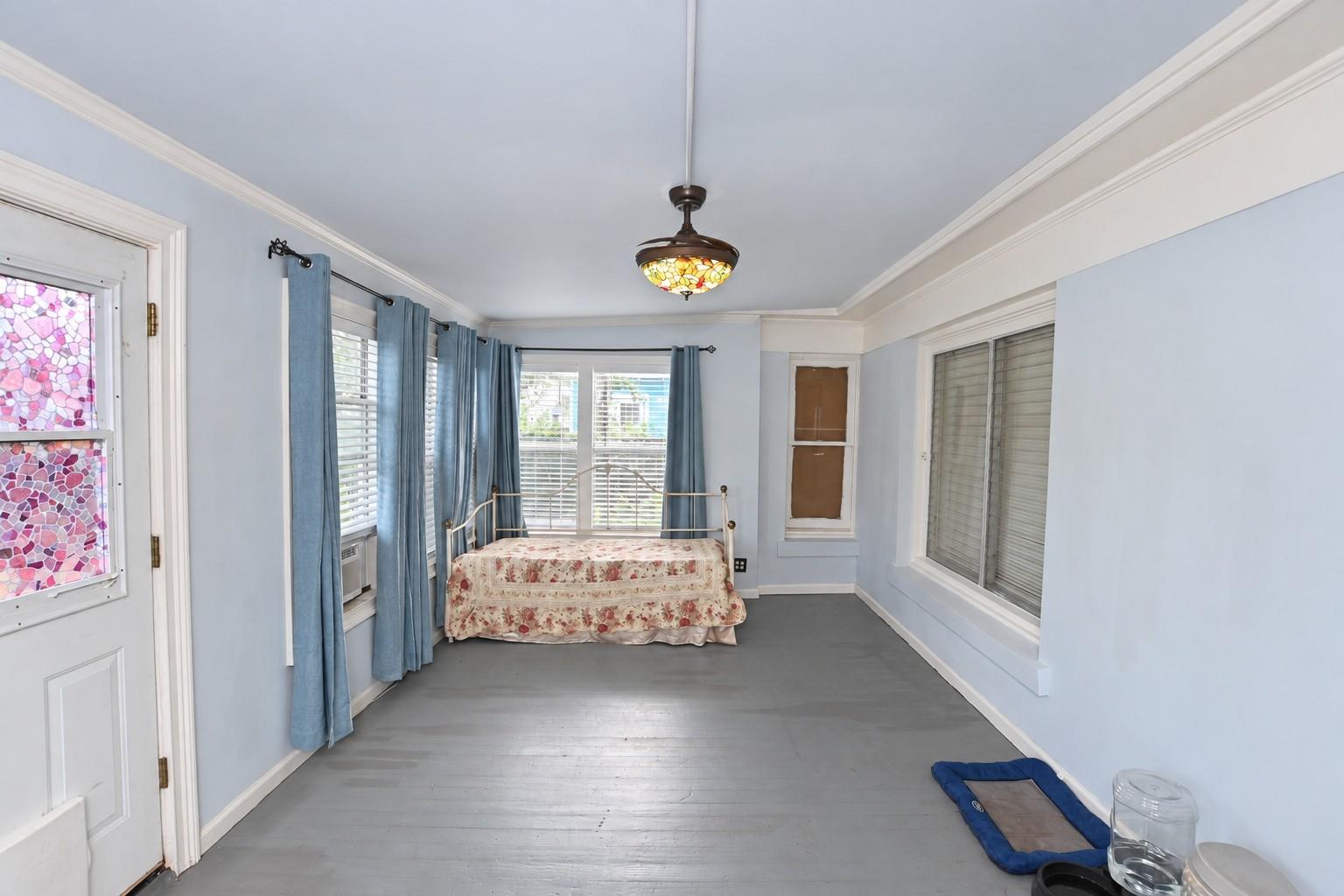 Bedroom with a floral-covered bed, blue curtains, and a stained-glass ceiling fan light.