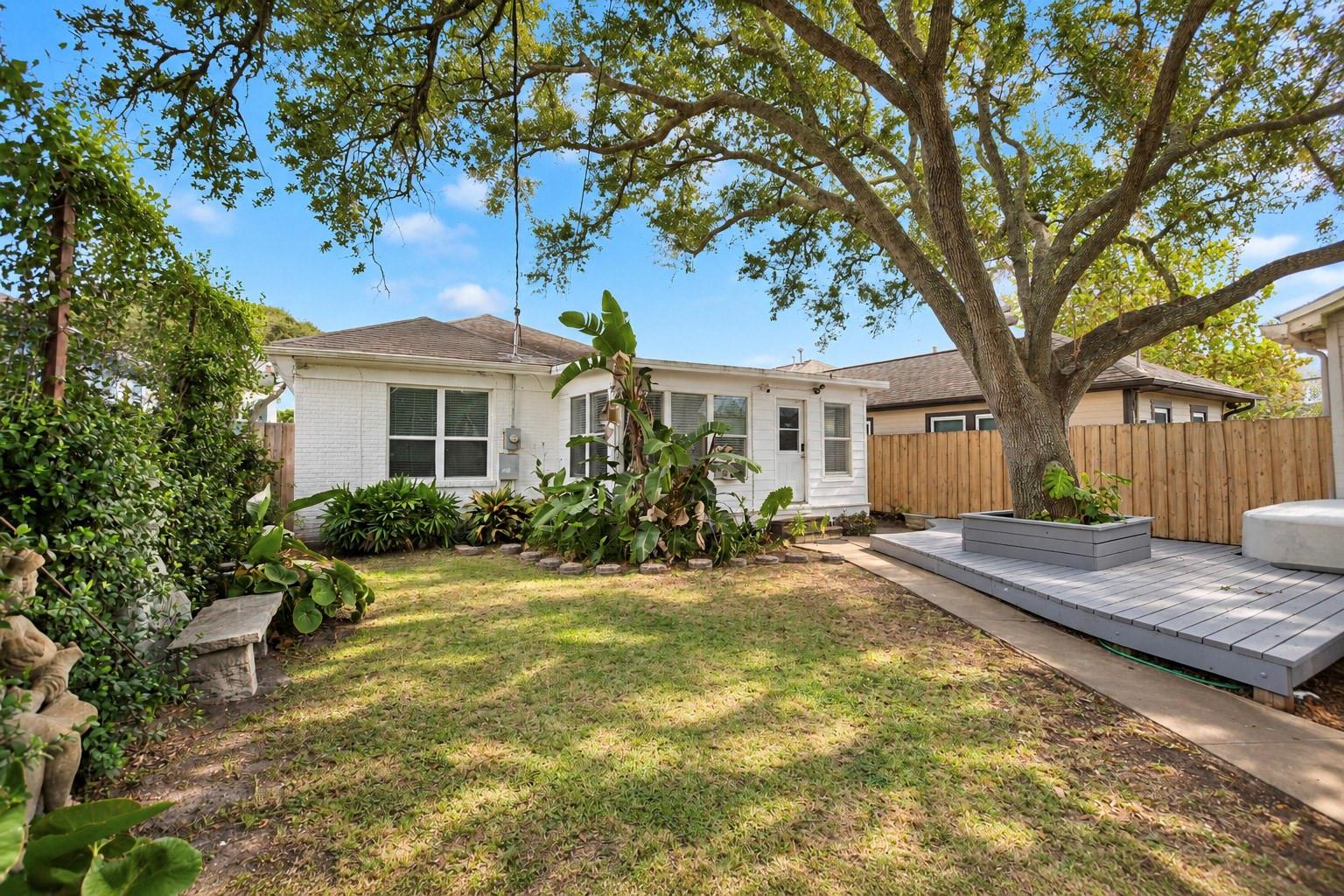White brick home and fenced backyard with a large shade tree and raised deck.