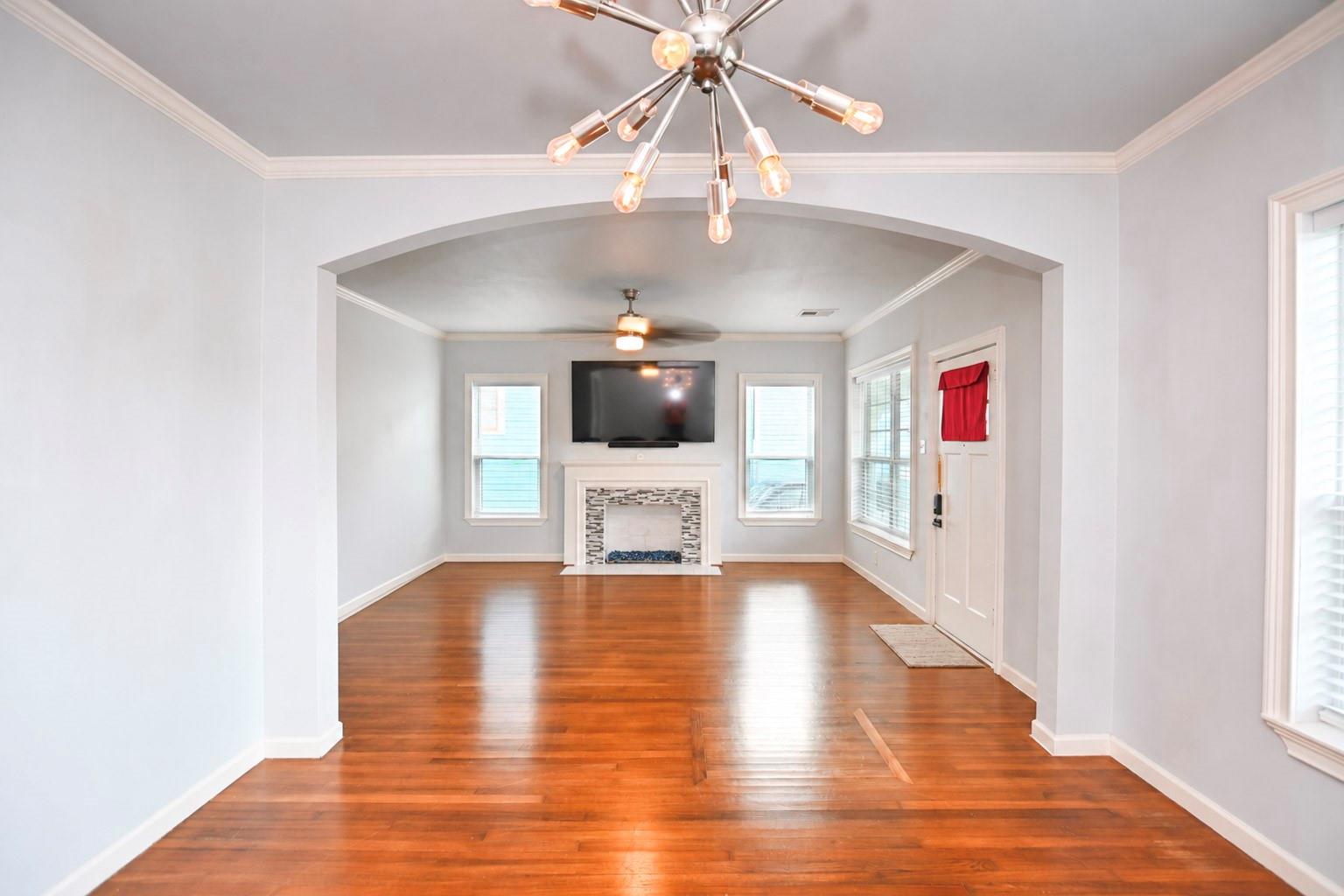 Living room with polished hardwood floors, an arched opening, and a fireplace beneath a mounted television.