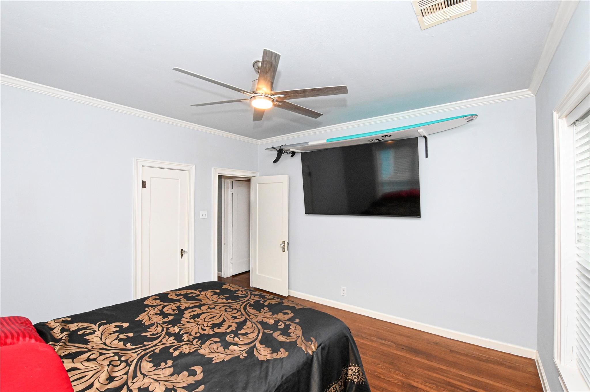 Bedroom with black-and-gold bedding, hardwood floors, and a surfboard mounted above the television.