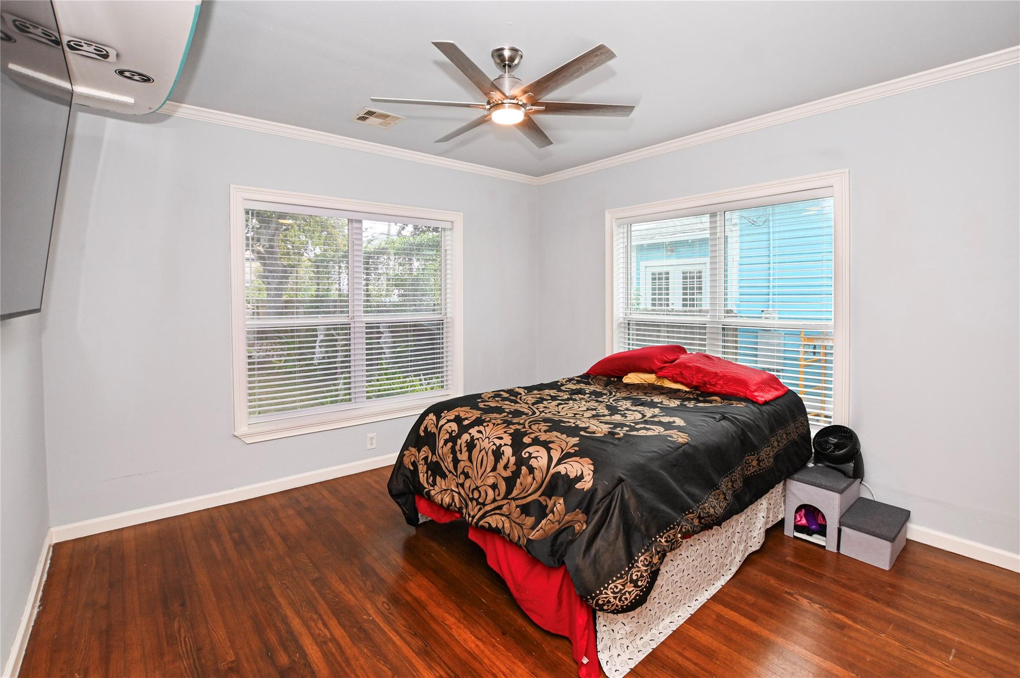 Furnished bedroom with a black-and-gold bedspread, two windows, and polished wood floors.