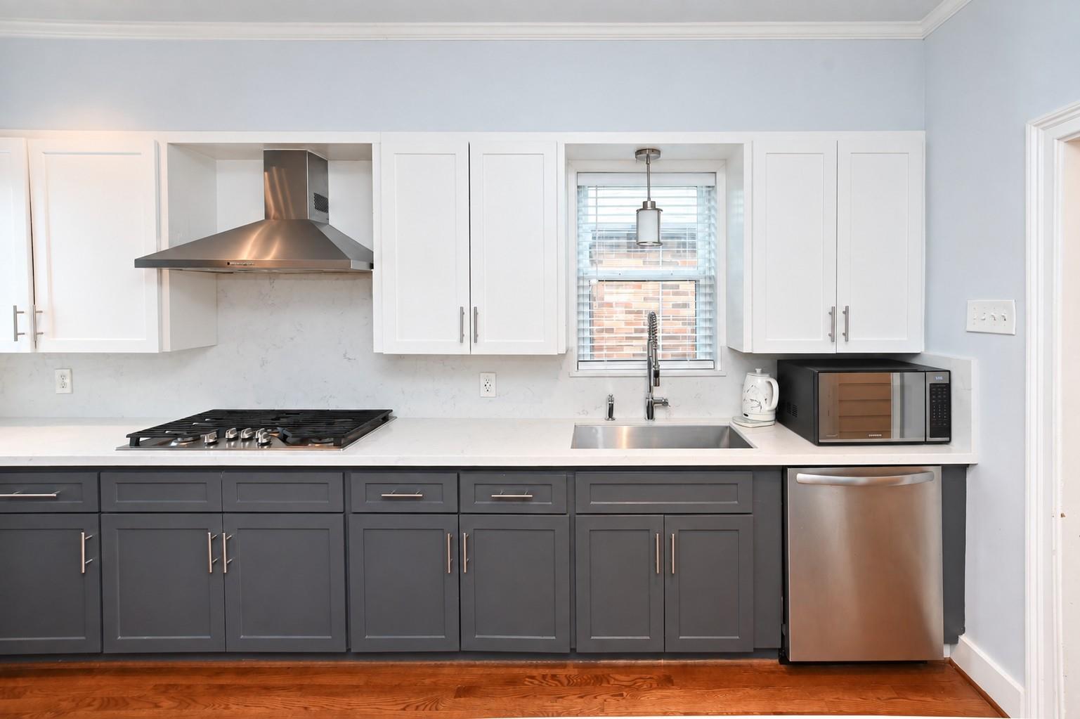Kitchen with dark gray cabinets, white counters, stainless steel appliances, and a window above the sink.