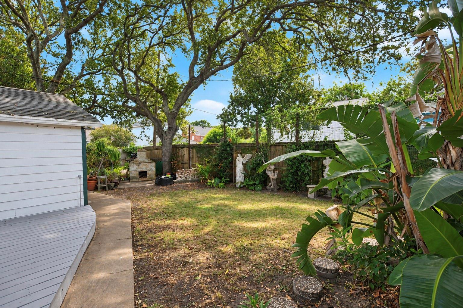 Shaded backyard with a large tree, banana plants, brick fireplace, and curved white deck.