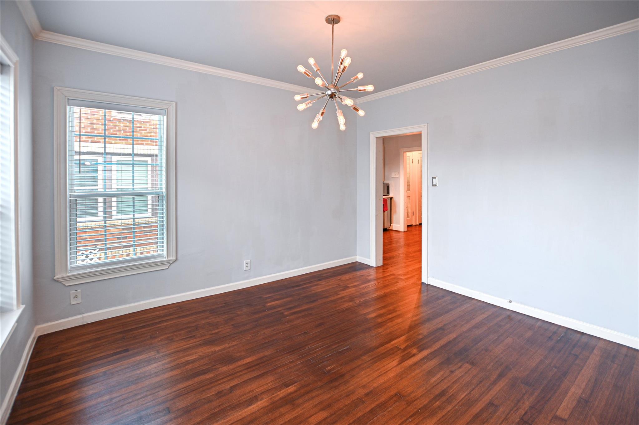 Empty room with dark hardwood floors, pale blue walls, and a starburst chandelier.