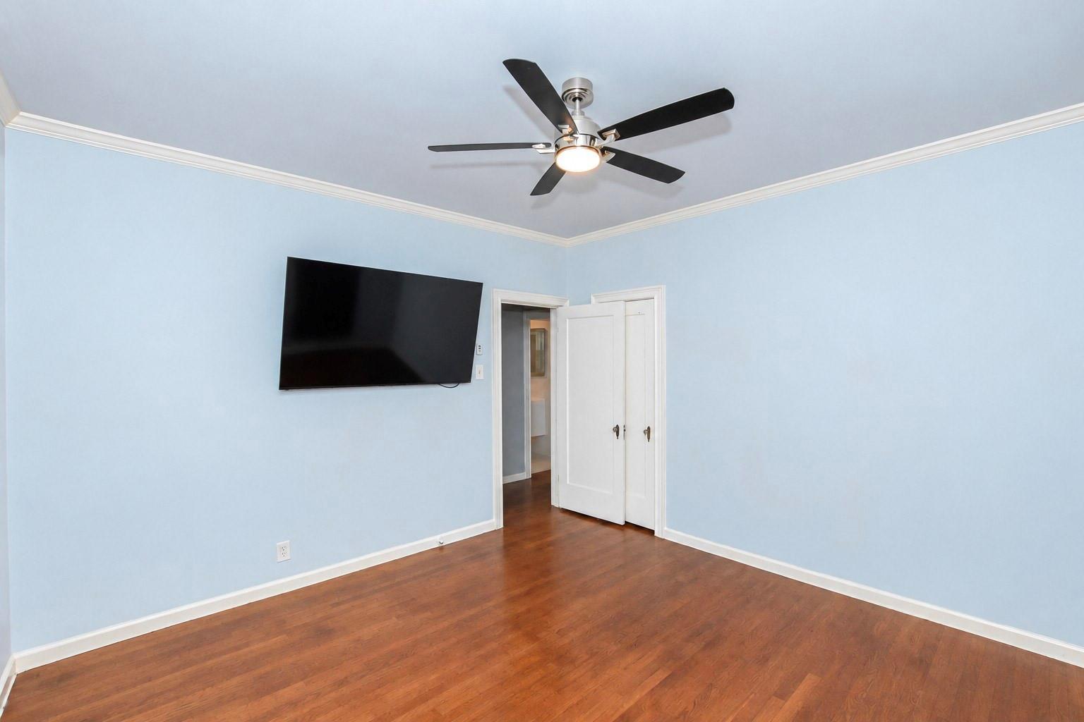 Empty blue-walled room with hardwood floors, a ceiling fan, and wall-mounted television.
