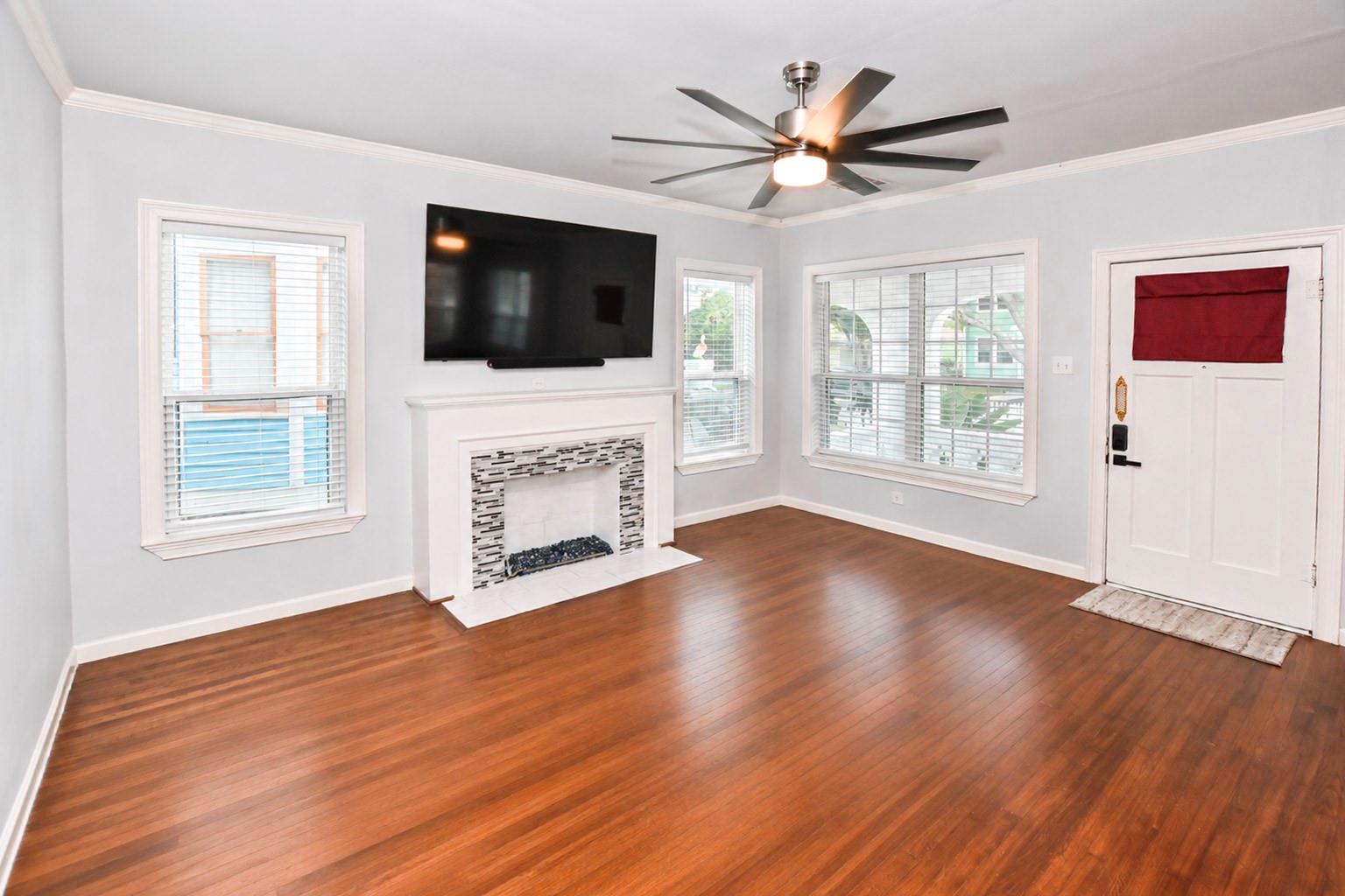 Unfurnished living room with hardwood floors, tiled fireplace, wall-mounted television, and large ceiling fan