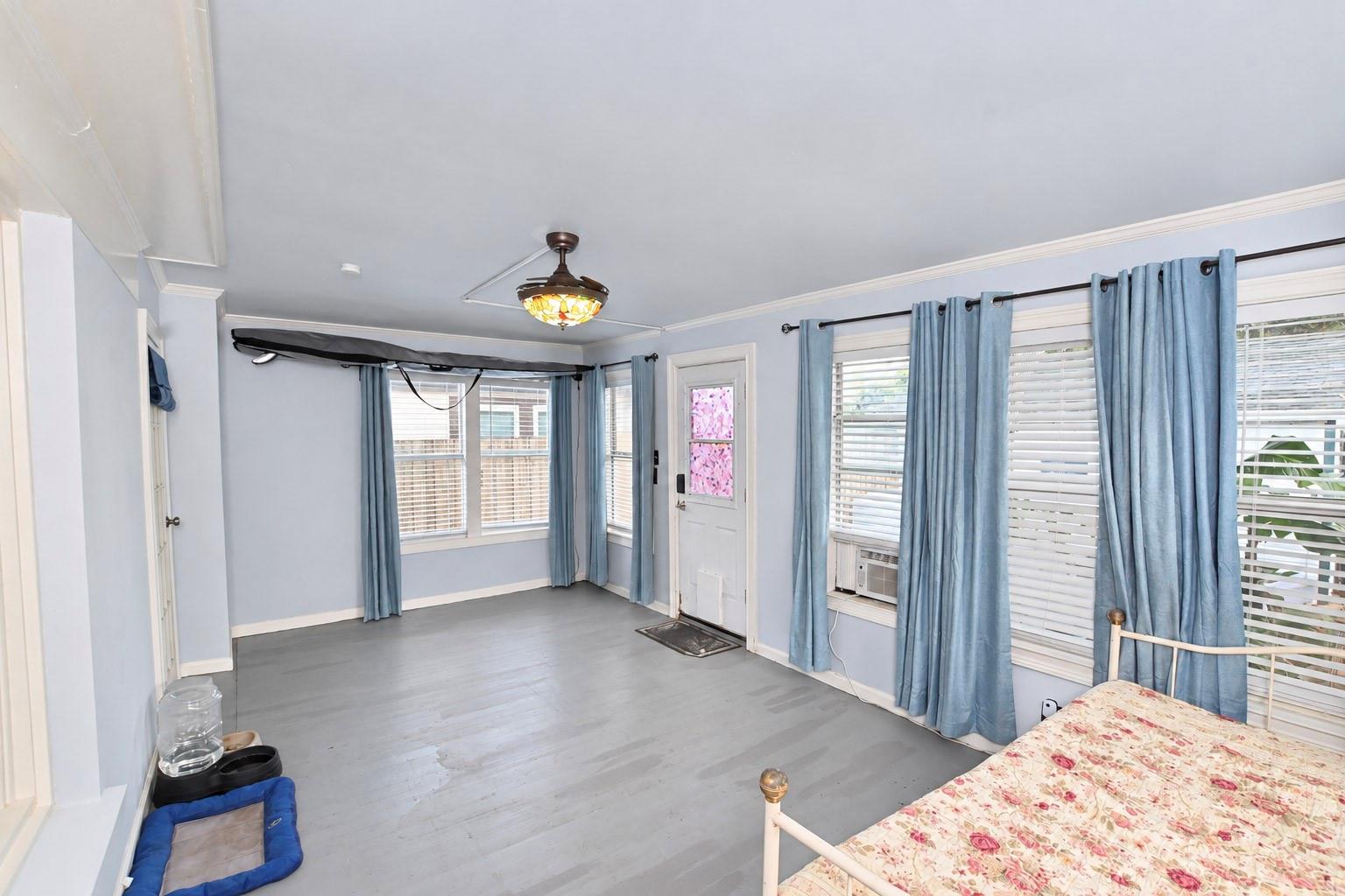 Bedroom with blue curtains, gray flooring, a floral bed, and a ceiling fan.
