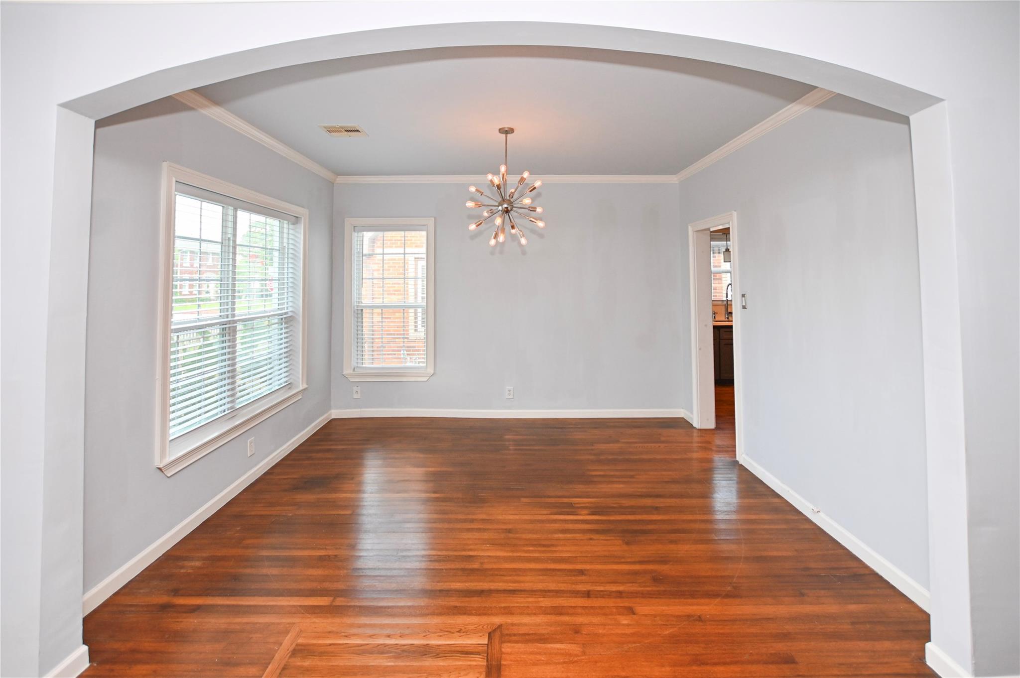 Empty dining room with hardwood floors, a broad archway, and a starburst chandelier.
