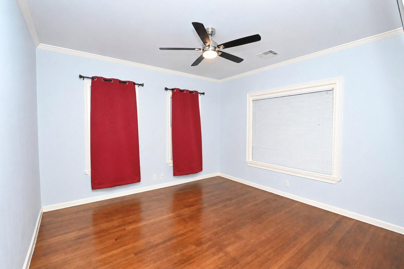 Empty room with hardwood floors, pale blue walls, red curtains, and a ceiling fan.