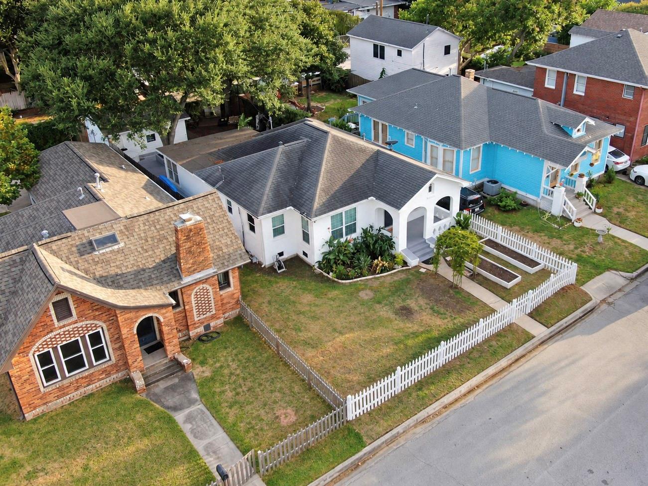 Aerial view of a white home with an arched porch and fenced front yard.