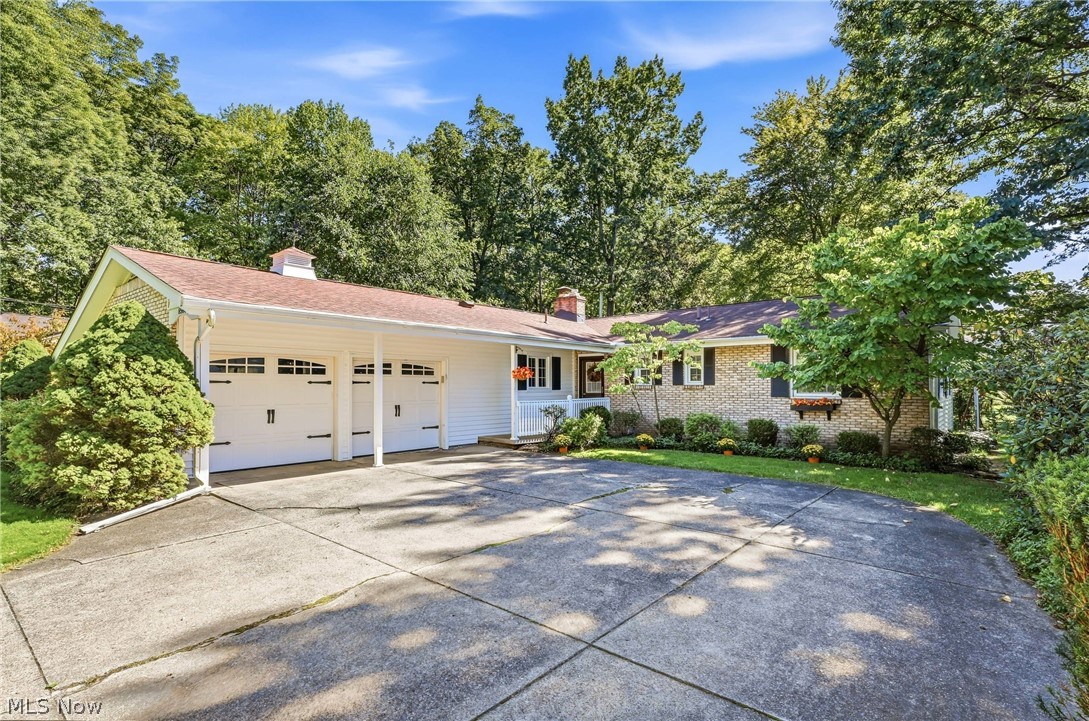 Ranch-style home with two white garage doors, a wide driveway, and mature trees.