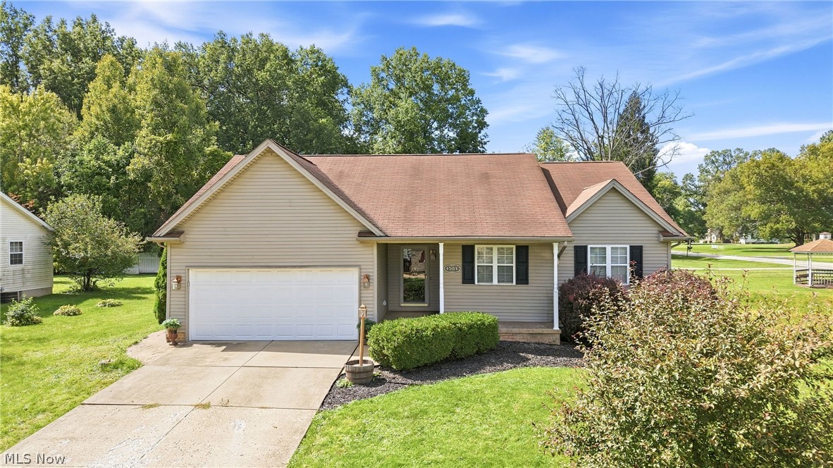 Single-story beige home with an attached garage, gabled roof, and landscaped front lawn.