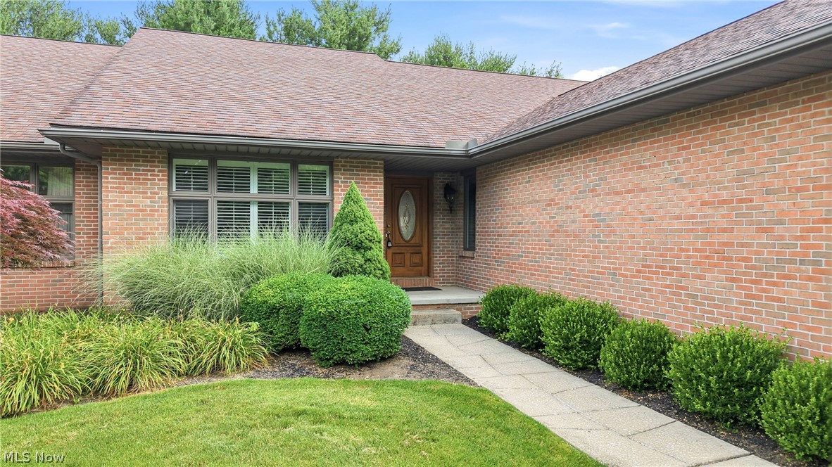 Red-brick home entrance with a wooden door, large windows, and a landscaped walkway.