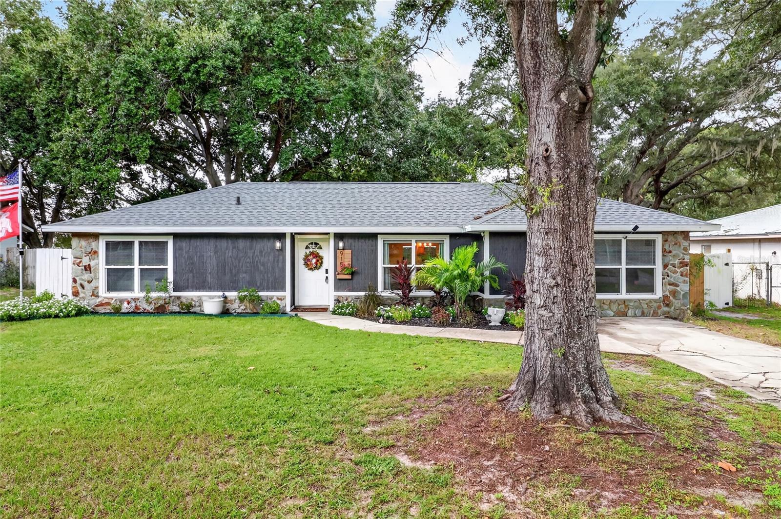 Single-story gray home with stone accents, landscaped lawn, and a large oak tree in front.