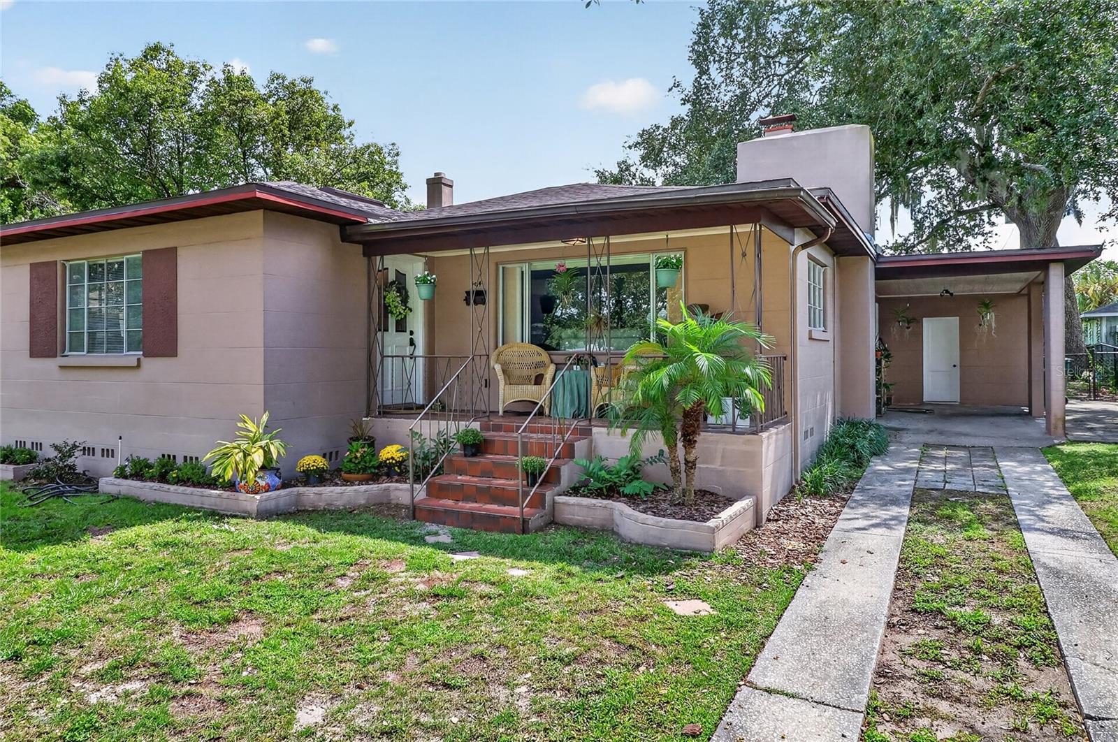 Single-story home with a covered porch, red-tile steps, hanging plants, and a covered carport.