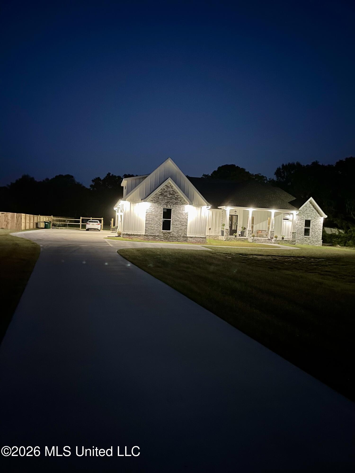 Light-sided and stone home with illuminated gables and a covered porch at night.