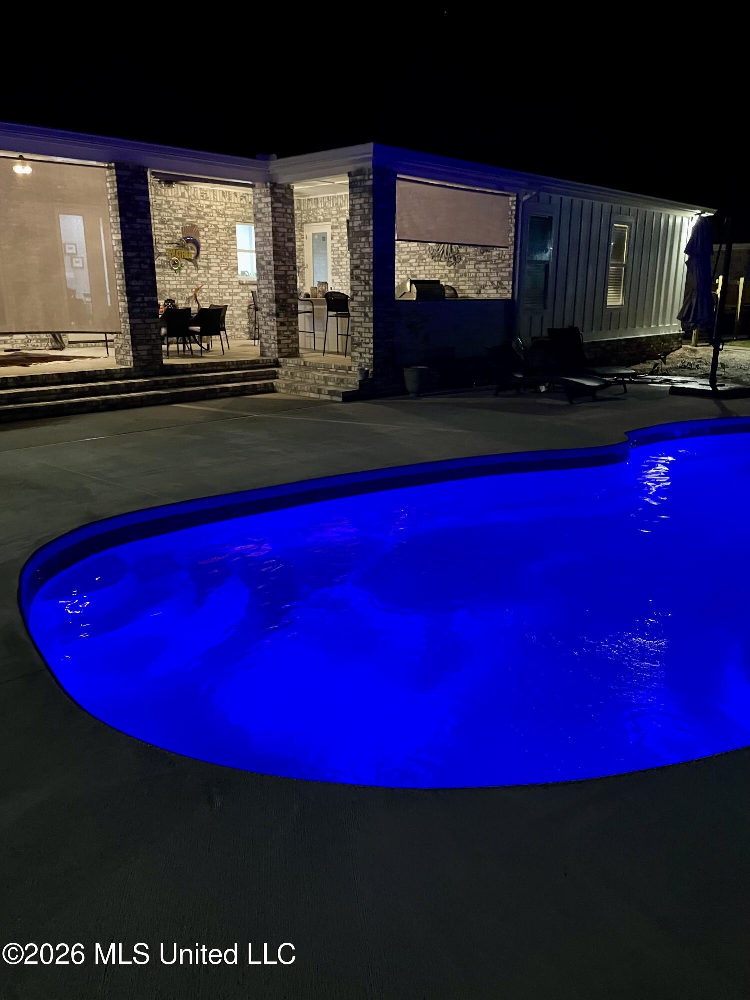 Blue-lit backyard pool beside a covered brick patio at night.